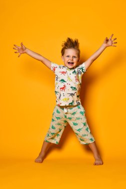 Dinazorlar ile pijama küçük sevimli sarışın çocuk okul öncesi sarı arka plan üzerinde stüdyoda sevinç var.