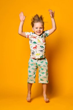 Dinazorlar ile pijama küçük sevimli sarışın çocuk okul öncesi sarı arka plan üzerinde stüdyoda sevinç var.