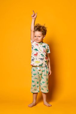 Dinazorlar ile pijama küçük sevimli sarışın çocuk okul öncesi sarı arka plan üzerinde stüdyoda sevinç var.