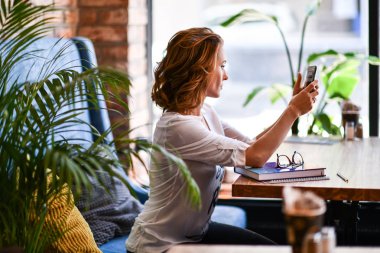 Bir kafede dinlenirken cep telefonuyla konuşan genç kadın, mavi bir koltukta otururken, boş zamanlarında bir kafede dinlenirken.