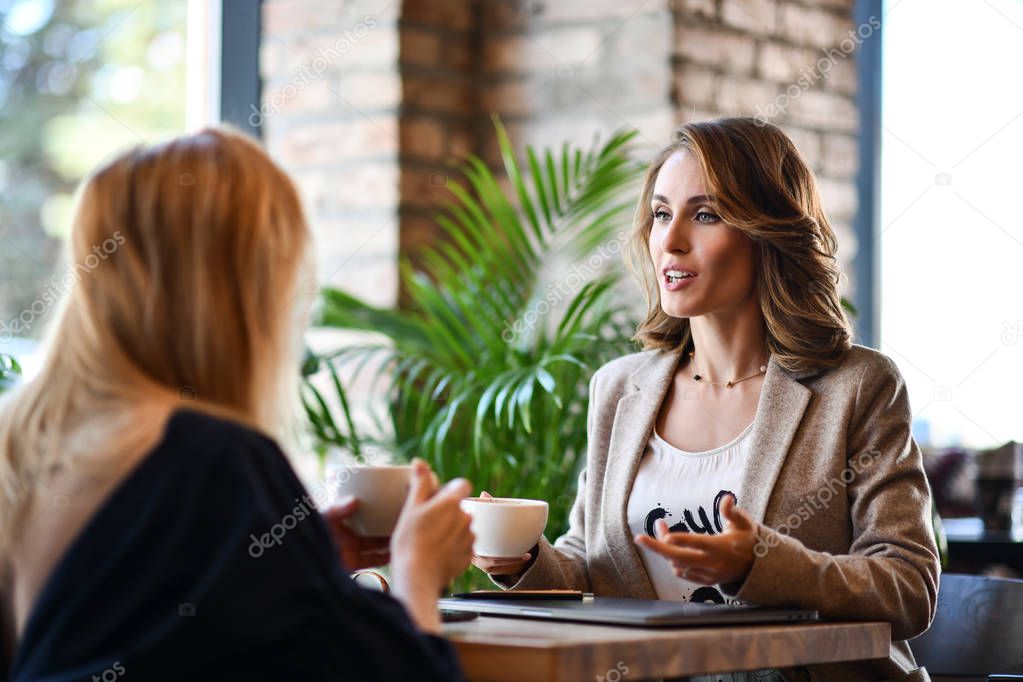 Two young business woman sitting at a table in a cafe. Girls communicate and discuss matters. Friendly meeting. Communication with a colleague