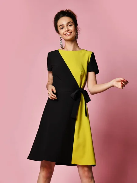 Feliz hermosa mujer joven en elegante vestido de cóctel negro está gritando, mirando a la cámara y señalando. Estudio de tres cuartos de duración sobre fondo rosa . —  Fotos de Stock