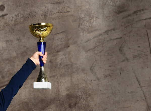 Close-up human hand holding golden Trophy on concrete background