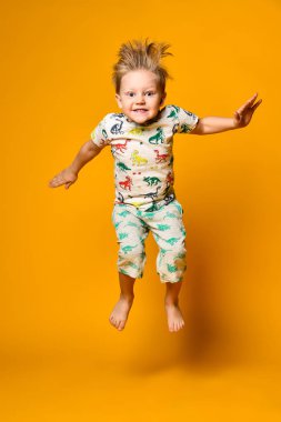 Dinazorlar ile pijama küçük sevimli sarışın çocuk okul öncesi sarı arka plan üzerinde stüdyoda sevinç var.