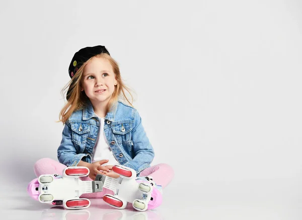 Meisje zit op de rollen in een blauwe denim en PET en glimlacht. Zomersporten voor kinderen. — Stockfoto