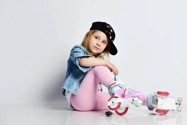Meisje zit op de rollen in een blauwe denim en PET en glimlacht. Zomersporten voor kinderen. — Stockfoto