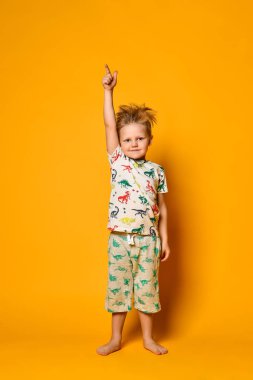 Dinazorlar ile pijama küçük sevimli sarışın çocuk okul öncesi sarı arka plan üzerinde stüdyoda sevinç var.