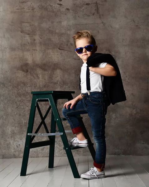Sevimli şık çocuk beton duvarın yanında sandalyede oturan — Stok fotoğraf