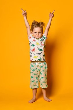 Dinazorlar ile pijama küçük sevimli sarışın çocuk okul öncesi sarı arka plan üzerinde stüdyoda sevinç var.