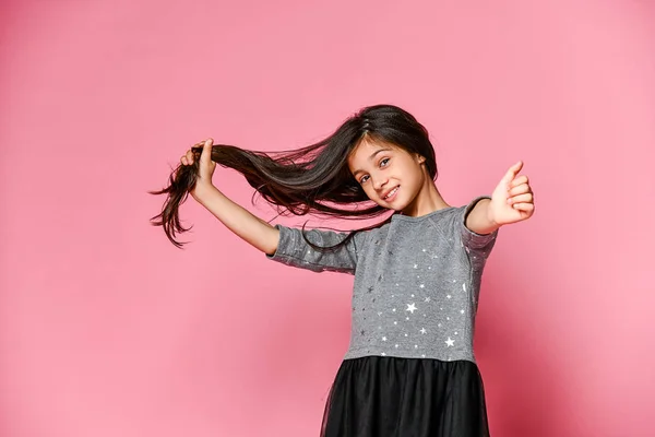 Kleine brunette meisje met lang haar houdt een streng van haar haar en toont de klas met haar duim. Wat lang haar deed ze groeien — Stockfoto