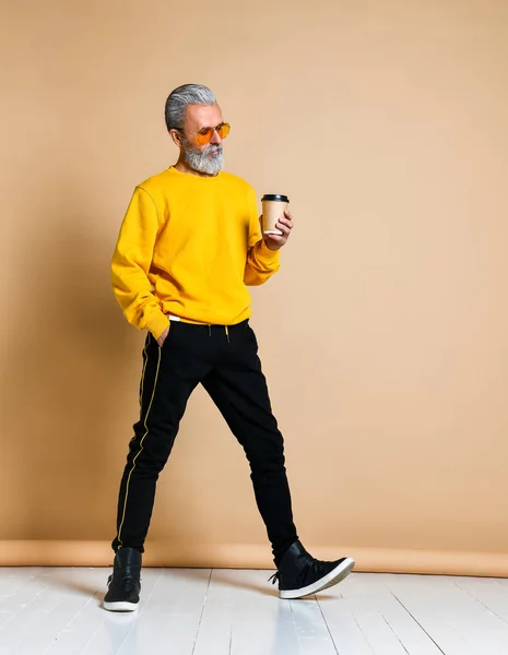 Fotografía vertical de un jubiloso anciano sosteniendo una taza de café blanco y mirando a la cámara — Foto de Stock