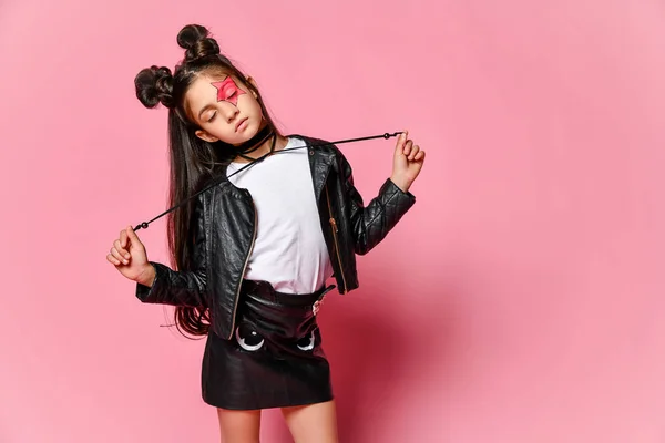 Menina hipster em uma jaqueta de couro preto posando em um fundo rosa, segurando os laços do colar . — Fotografia de Stock