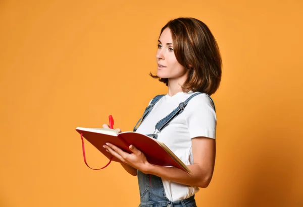 Pretty young beautiful woman standing, writing, take notes, holding textbook notebook organizer in hand and pen — Stock Photo, Image
