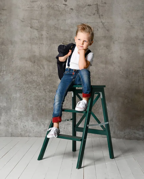 Cute stylish boy sitting on chair near concrete wall — Stock Photo, Image