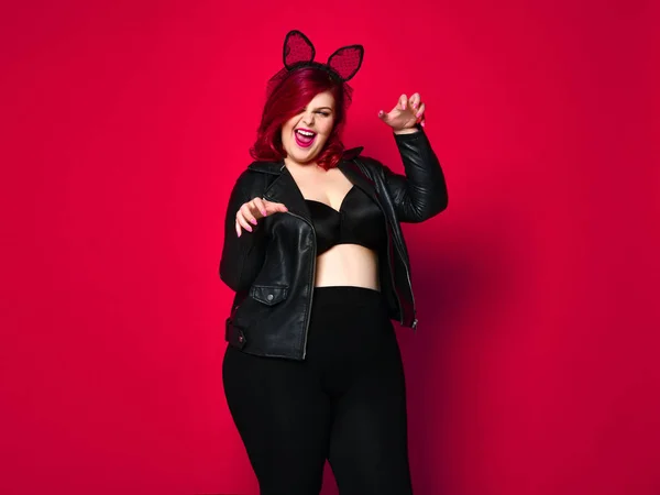 Niedlich sexy plus size Brünette mit schwarzen Hasenohren in Lederjacke und Unterwäsche posiert auf rotem Hintergrund — Stockfoto