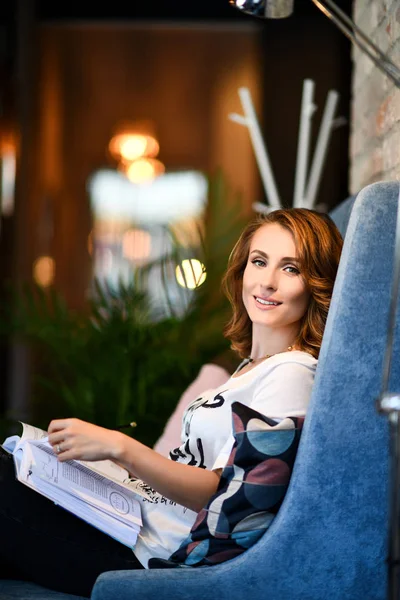 Dreamy young beautiful woman writes future plans and goals in her diary, relaxing in a cozy dining room reading a book. Smiling girl looks at you in camera.