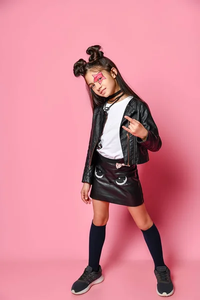 Retrato de una pequeña chica hipster en una chaqueta de bombardero y minifalda, mostrando un letrero de yo con los dedos, la infancia de moda — Foto de Stock