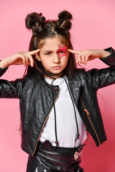 Portret van een hipster punk meisje-gekleed in een leren jas en rok, zwarte knie-highs en een wit T-shirt, met een grappig kapsel en een make-up geschilderde ster op het gezicht, wijst op het hoofd. — Stockfoto