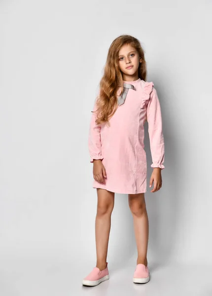 Όμορφο μικρό κορίτσι με μακριά ξανθά μαλλιά και μπλε μάτια, στέκεται σε ένα λευκό φόντο, φορώντας ένα ροζ casual φόρεμα και παπούτσια γυμναστήριο, Έφηβος στυλ — Φωτογραφία Αρχείου