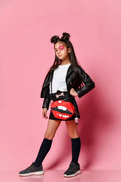 Pequeña chica hipster punk de moda vestida con una chaqueta y falda de cuero, loaches negros y una camiseta blanca, con un peinado divertido y una estrella de maquillaje pintada en su cara. — Foto de Stock