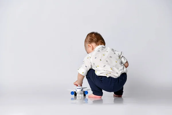 Little toddler boy sits back on a light wall background in an empty room with a toy airplane — Stock Photo, Image