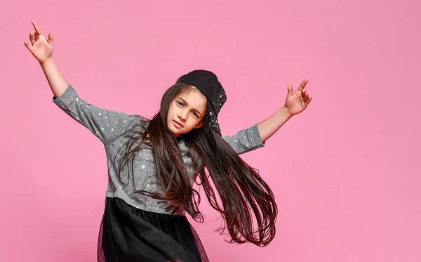 Portret van een klein hippie meisje in een donkere jurk met een honkbalpet en sneakers, op een roze achtergrond — Stockfoto