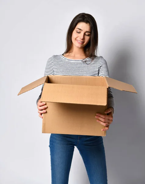Όμορφη μελαχρινή γυναίκα στέκεται σε ένα ελαφρύ φόντο με ένα κινούμενο κουτί από χαρτόνι — Φωτογραφία Αρχείου