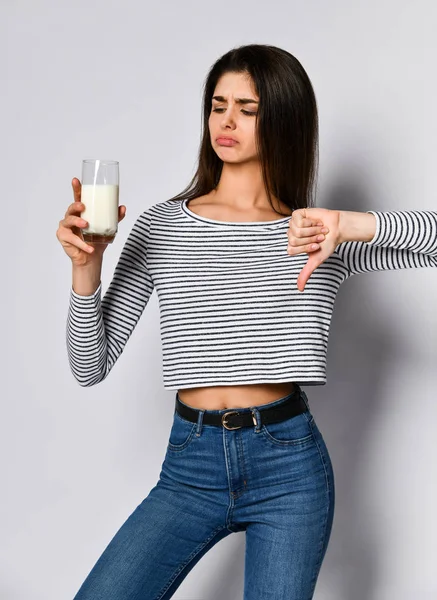 Missnöjd ung kvinna hålla ett glas med komjölk och visar en dålig tumme tecken ner — Stockfoto