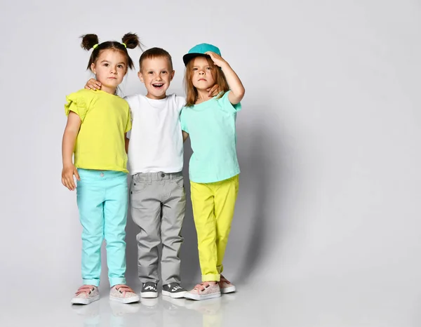 Studio portrait of children on a light background: full body shot of three children in bright clothes, two girls and one boy. Triplets, brother and sisters. — Stock Photo, Image