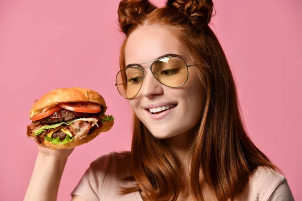 Žena jíst burger sendvič s hladovými ústy na růžovém pozadí. — Stock fotografie