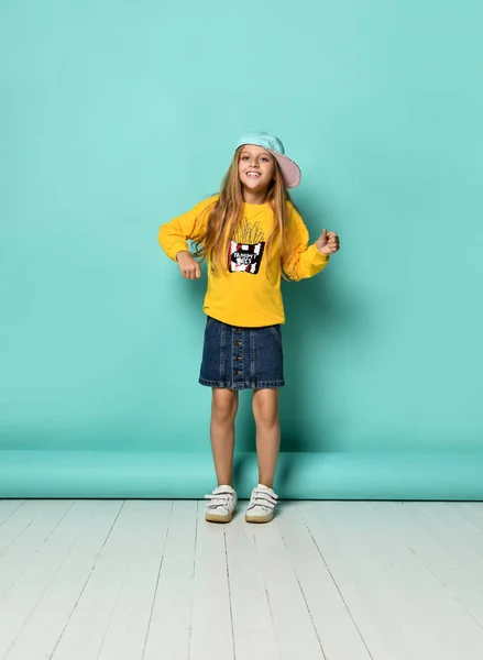 Mooie modieuze jonge tiener met een mooie glimlach poseren in een honkbalpet en gele hoodie op een blauwe achtergrond — Stockfoto