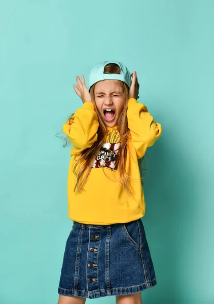 Pretty fashion young teenager with a lovely smile posing in a baseball cap and yellow capodie on a blue background — Stock fotografie