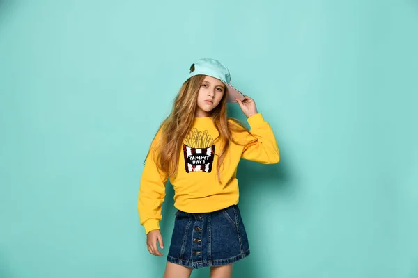 Engraçado adolescente menina em um boné de beisebol e capuz amarelo posando em um fundo azul . — Fotografia de Stock