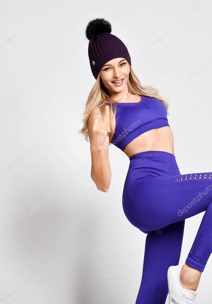 Beautiful Athletic girl working standing in blue sportswear on a light background rejoices at the end of the workout and her beautiful body. Victory