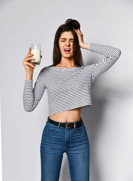 Spännande ung kvinna som håller i ett glas mjölk, utan att veta om hon ska dricka den eller inte. — Stockfoto