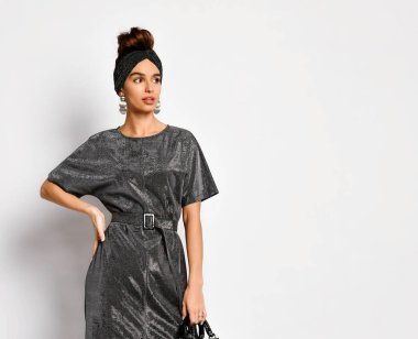 Saçları updo şeklinde, orijinal saç bandı, küpe ve kömür rengi elbiseyle poz veren çekici bir manken. Bel portresi beyaza izole edilmiş. Boşluğu kopyala