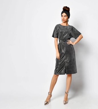 Şık saç bandı ve parlak kömür elbisesiyle poz vermiş, kemer takmış, eli kalçasında, beyaz tenli güzel bir kadın.