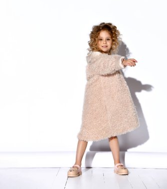 Altın kolyeli, tüylü pembe elbiseli, kürklü, ayakkabılı küçük sarışın manken. Ellerini aç, gülümse, bembeyaz poz ver.