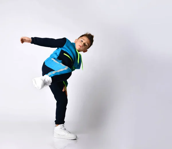 Een jongen in een kleurrijk trainingspak, sneakers. Hij schopt met zijn been, poseert geïsoleerd op een witte achtergrond. — Stockfoto