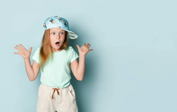 穿T恤、裤子和帽子的孩子，用菠萝印刷。她举起双手，在碧绿的背景下摆出一副震惊的样子。靠近点 — 图库照片
