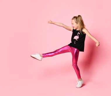 Siyah tişörtlü ve parlak taytlı kaprisli kız yüksek sesle bağırıyor, tekmeliyor ve yumrukluyor. Tam uzunlukta çekim pembe üzerinde izole edildi, kopyala boşluk