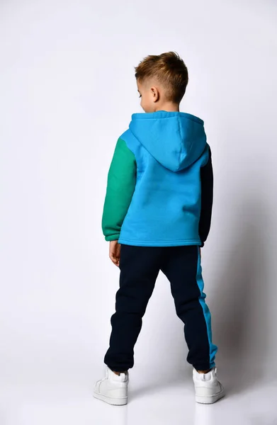 Niño en traje deportivo colorido, zapatillas de deporte. Miró hacia atrás, posando de pie frente a la cámara, aislado en un estudio blanco —  Fotos de Stock