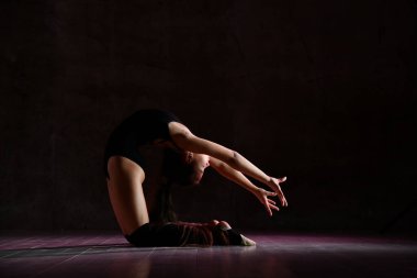 Siyah spor vücutlu genç bir jimnastikçi kız ve özel ayakkabılar siyah arka planda jimnastik pozu veriyor.