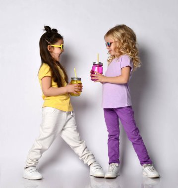 Two little girls in sunglasses, colorful casual clothes. Holding cocktail bottles, smiling, posing isolated on white. Childhood clipart
