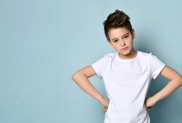 Brunet tienerjongen in wit t-shirt. Hij legde zijn handen op heupen en keek naar je, poserend tegen een blauwe studio achtergrond. — Stockfoto