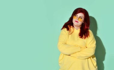 Aşırı kilolu düşünceli genç bayan şüpheyle el ele tutuşup göğsüne bakıyor. Kırpılmış stüdyo çekimi mavi üzerine izole edildi