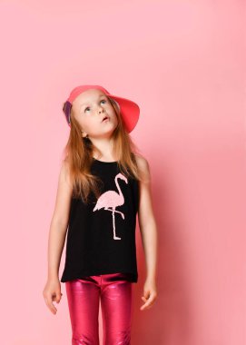 Flamingo ve parlak pantolonlu, modaya uygun siyah tişörtlü, düşünceli küçük bir kız. Pembe üzerine izole edilmiş üç çeyrek boyda portre.