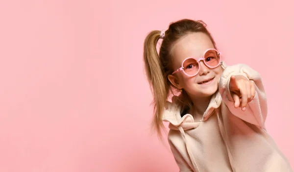 Glimlachende kleine meisje kleuter met pony verhaal naar voren wijzend wijsvinger naar je. Close-up schot geïsoleerd op roze, kopieerruimte — Stockfoto