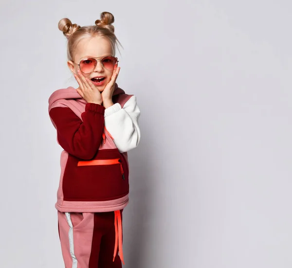 Bezorgd of bang klein meisje in stijlvol joggingpak en een zonnebril die kuikens met handen aanraakt. Portret geïsoleerd op lichtgrijs, kopieerruimte — Stockfoto
