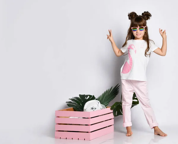 A beautiful girl poses next to a pink wooden box, wearing A Flamingo t-shirt and sunglasses Stock Photo